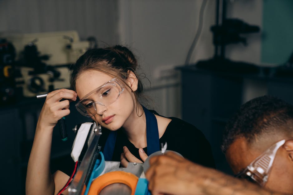 Young female engineer wearing goggles, adjusting machinery in an industrial workshop setting