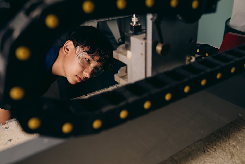 Young Asian engineer wearing goggles, inspecting machinery in a workshop setting